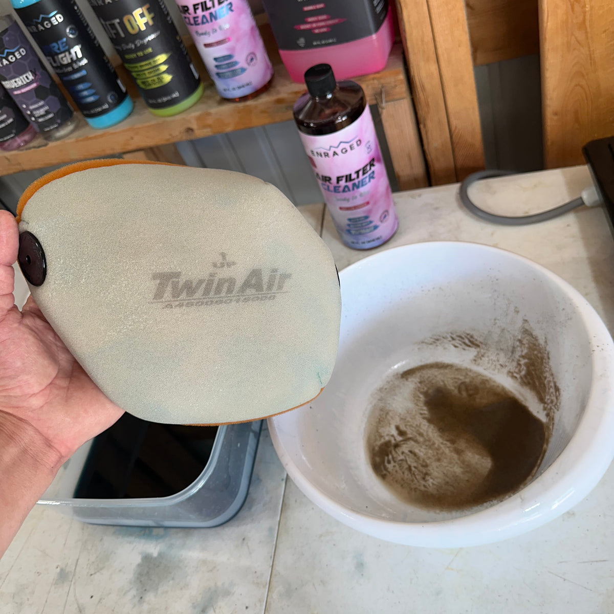Enraged Air Filter Cleaner beside a foam filter and a bowl of dirty wash water.